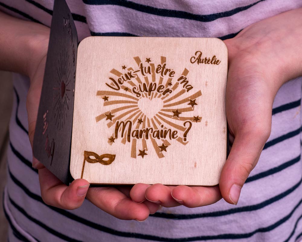 Carte bois demande marraine DHLaser Design gravee Veux-tu etre ma super Marraine prenom Aurelie tenue en main sur fond neutre