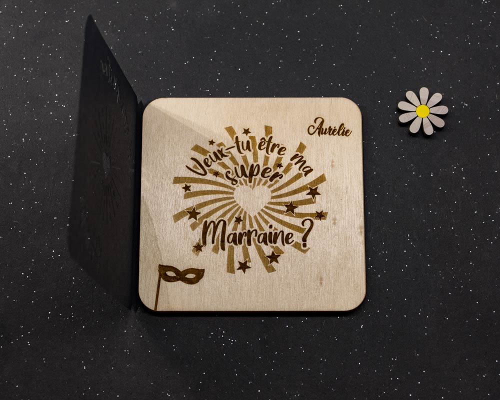 Carte bois demande marraine DHLaser Design prenom Aurelie gravure etoiles dorees presentee avec fleur et support noir sur fond sombre