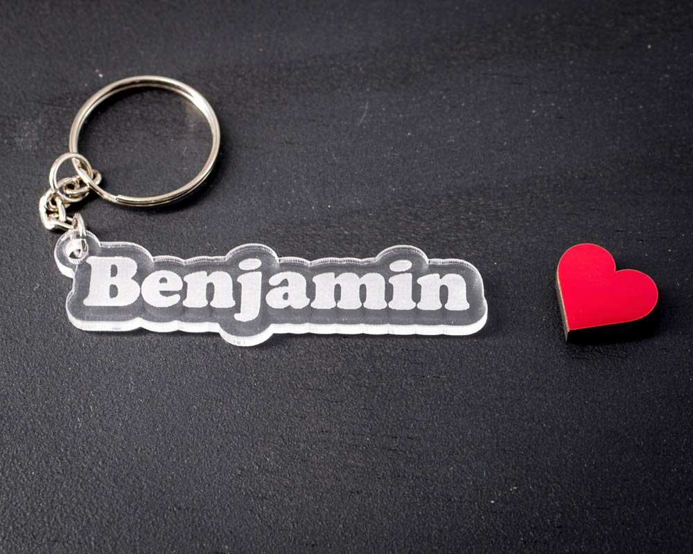 Porte-clé transparent personnalisable avec le prénom Benjamin découpé, anneau métallique argenté, posé sur fond noir par DHLaser Design